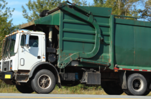 Green garbage truck in front of trees.