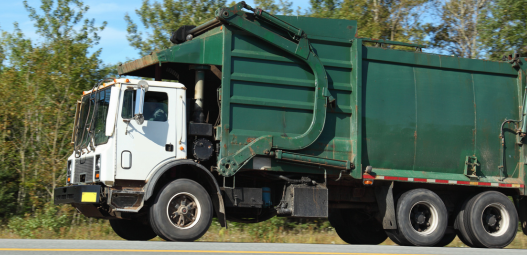 Green garbage truck in front of trees.